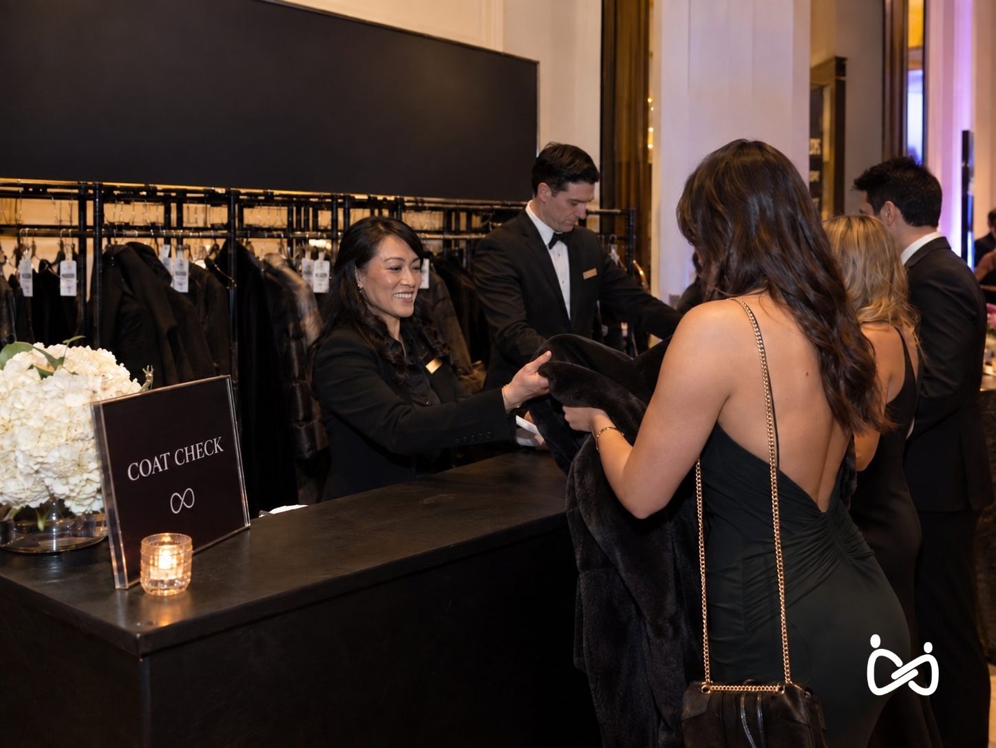 ServeSync coat check attendant handing a coat back to a guest at a branded coat check counter during an NYC event